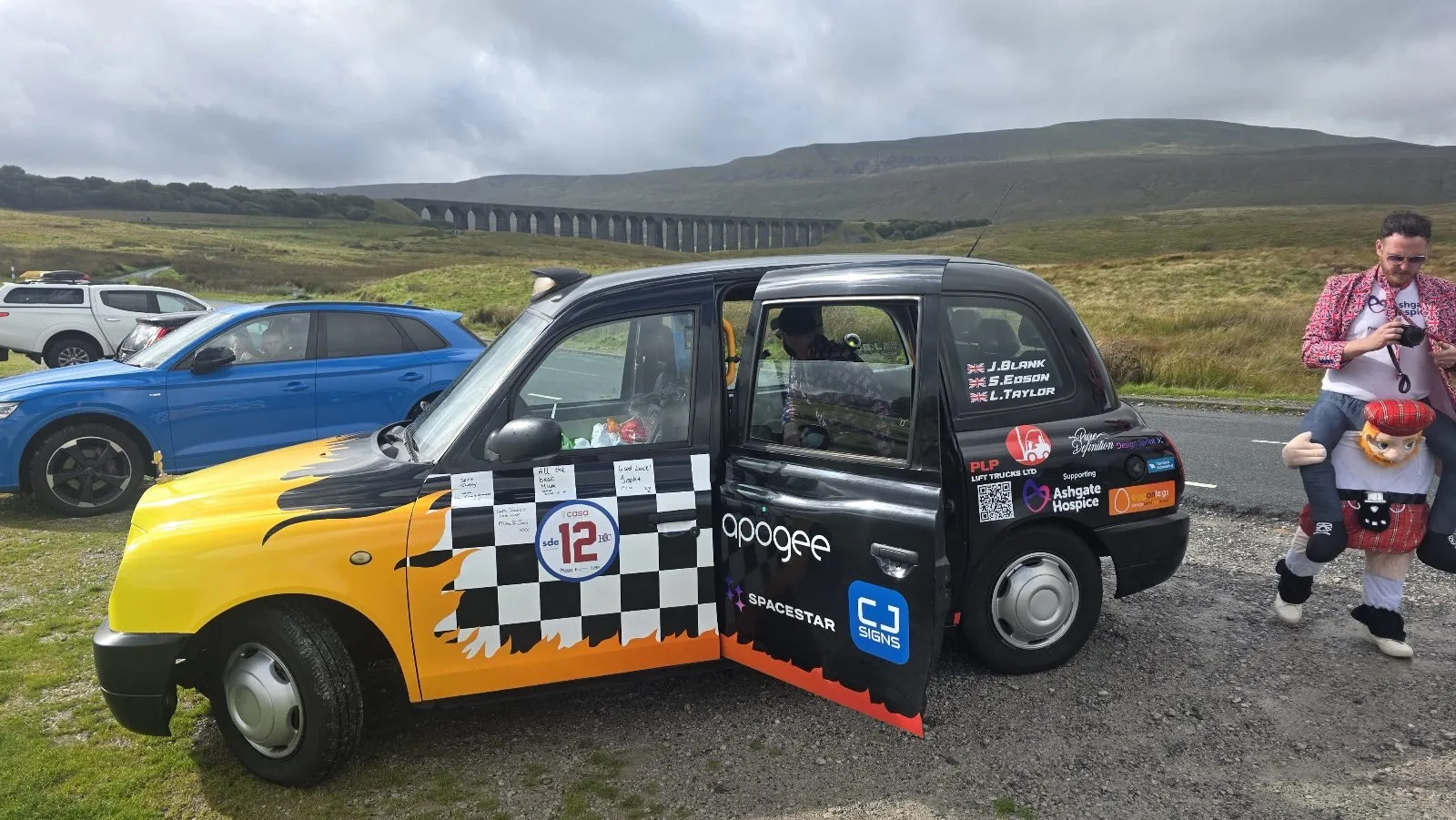 The taxi with its doors open in front of the Ribblehead Viaduct